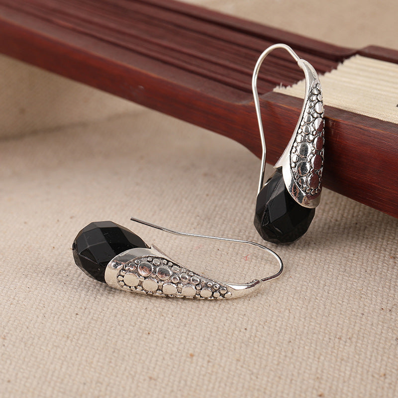 Vintage-inspired earrings with black gemstone and detailed metal carving – statement accessory.
